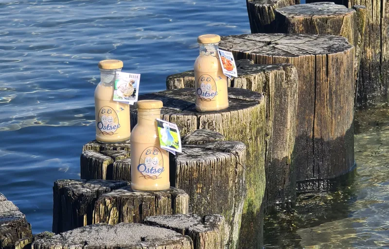 Drei Flaschen Eierlikör stehen auf den ins Wasser ragenden Buhnen, umgeben von ruhigem Wasser und maritimer Atmosphäre.