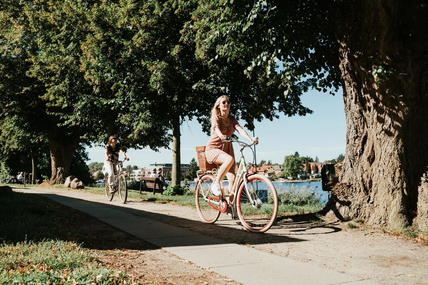 Zwei Frauen fahren mit ihren Fahrrädern auf einem Radweg entlang eines Sees.